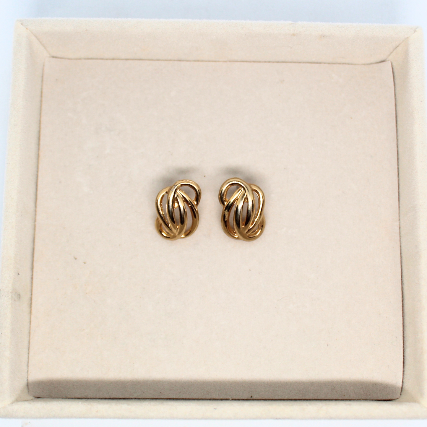 Pair of gold earrings on a beige jewelry display box