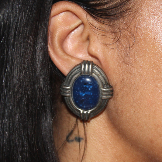 Close-up of an ear wearing a silver earring with a blue gemstone.