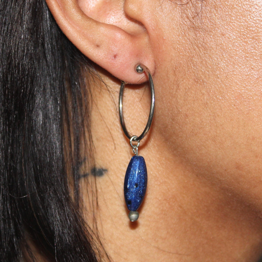Close-up of an ear wearing a hoop earring with a blue bead.