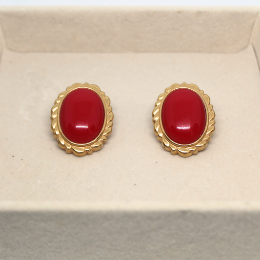 Pair of red earrings with gold settings on a beige background