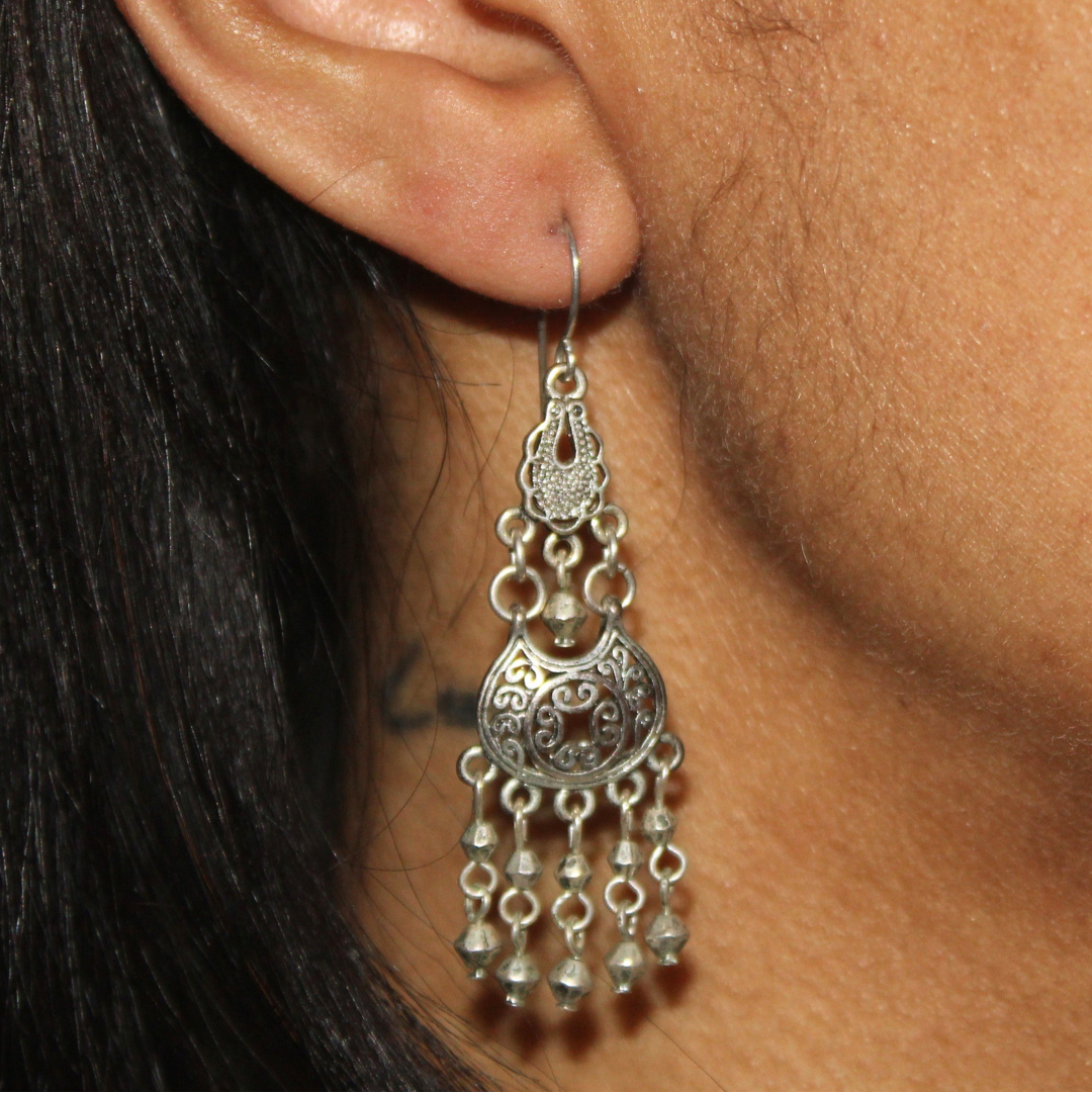 Close-up of an ear wearing a silver earring with dangling beads.