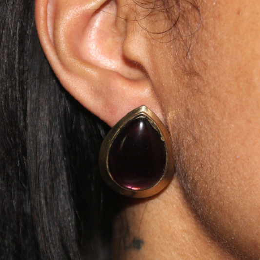 Close-up of an ear wearing a gold earring with a dark gemstone.