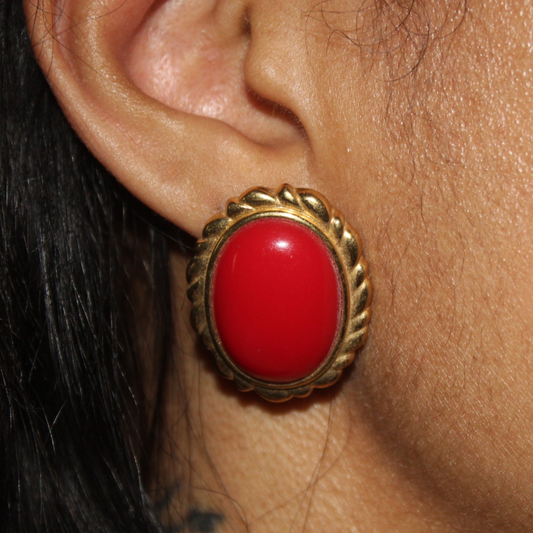 Close-up of a red earring with gold setting on an ear.