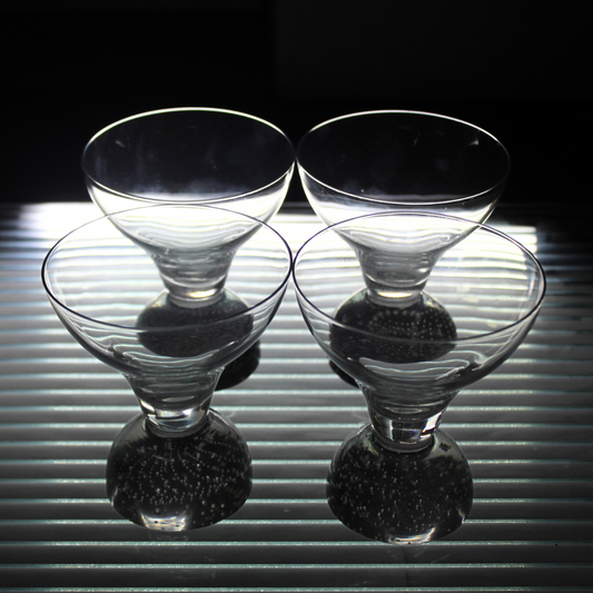 Four clear glass martini glasses on a reflective surface with a dark background