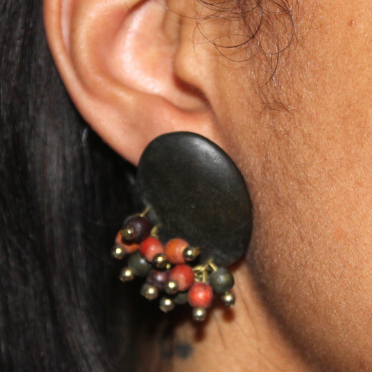 Close-up of an ear wearing a black earring with red and gold beads.