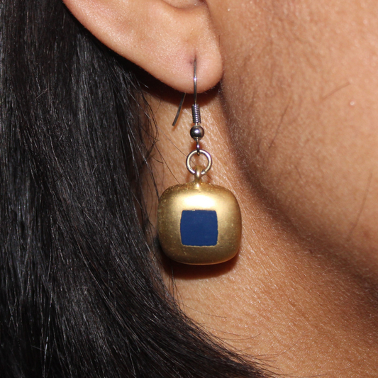 Gold earring with a blue square pendant worn by a person with dark hair.
