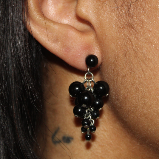 Close-up of an ear wearing a black beaded earring with a blurred background