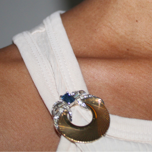 Close-up of a person wearing a white top with a decorative gold and blue brooch.