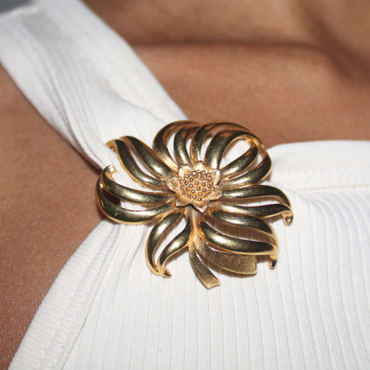 Gold flower-shaped brooch on a white garment with a blurred background