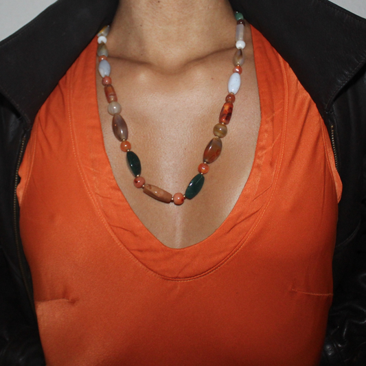 Person wearing an orange top and a colorful beaded necklace with a black jacket.