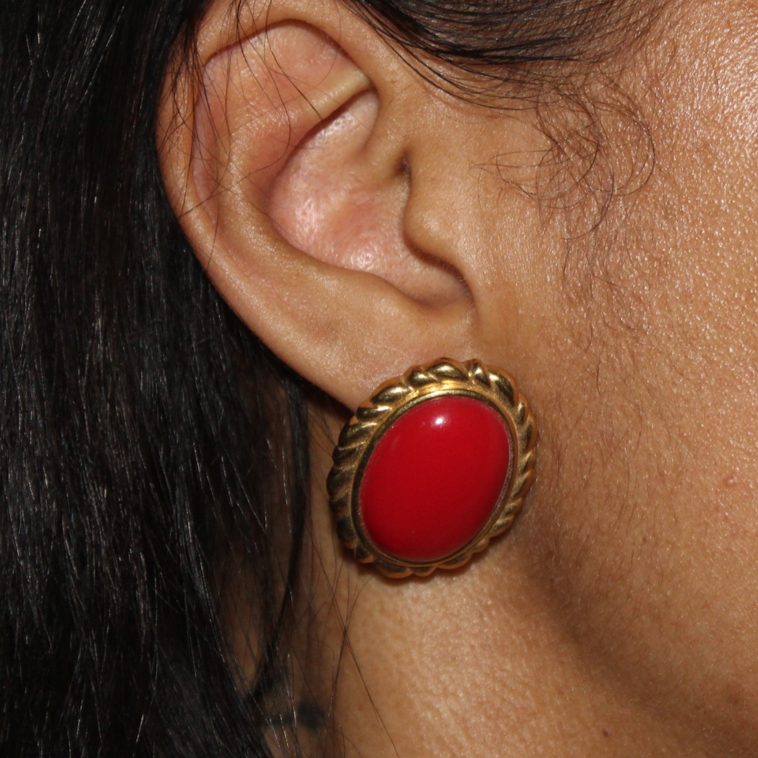 Close-up of an ear wearing a gold earring with a red gemstone.
