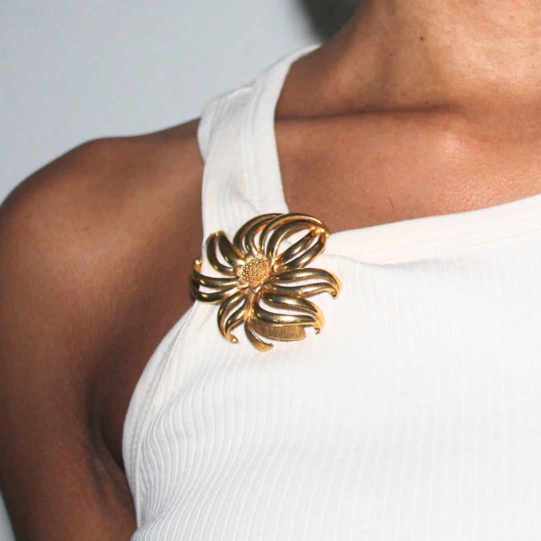 Gold flower-shaped brooch on a white dress against a neutral background