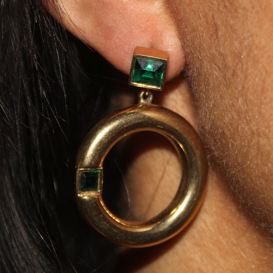 Gold earring with green gemstones worn by a person