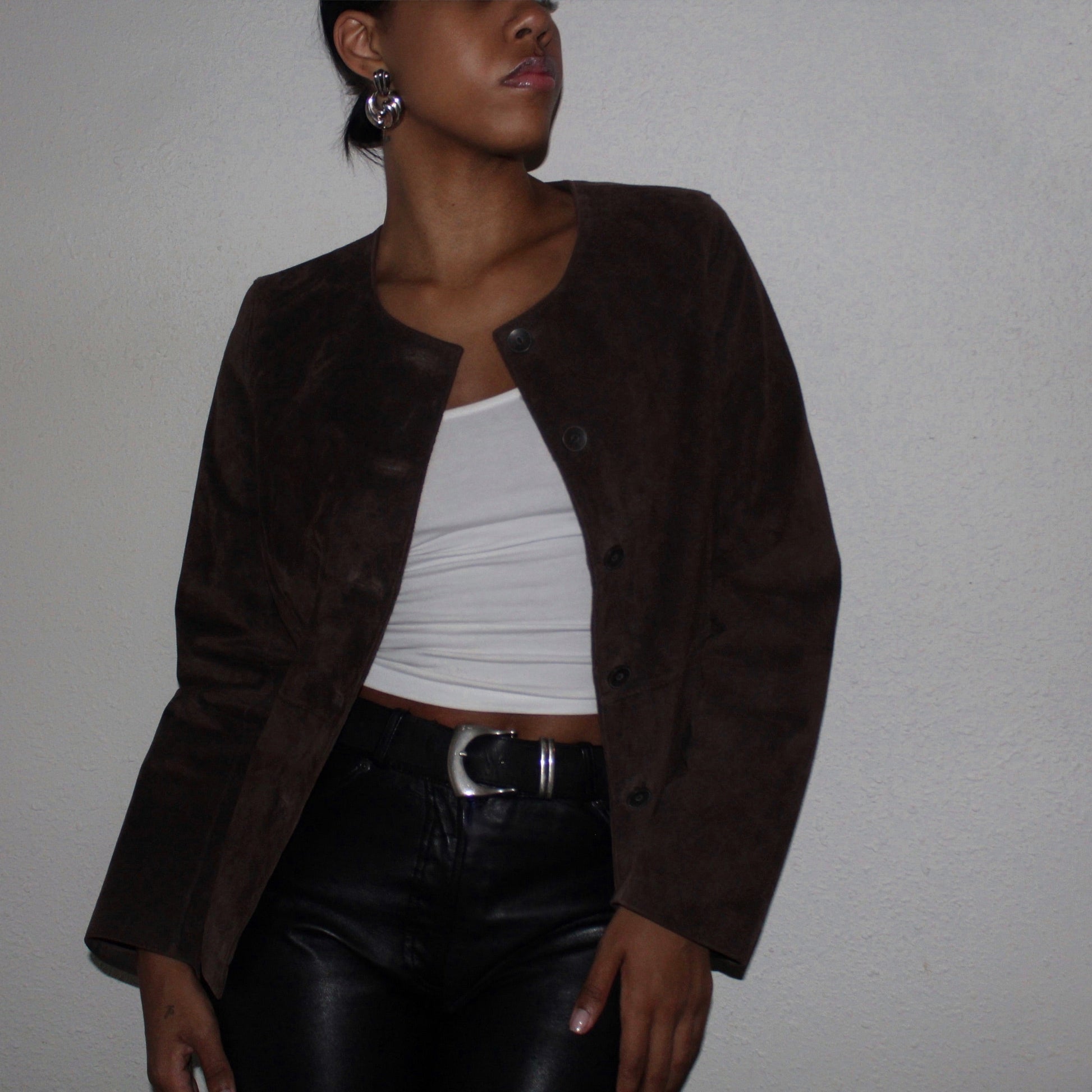 Person wearing a brown jacket over a white top and black pants against a plain background