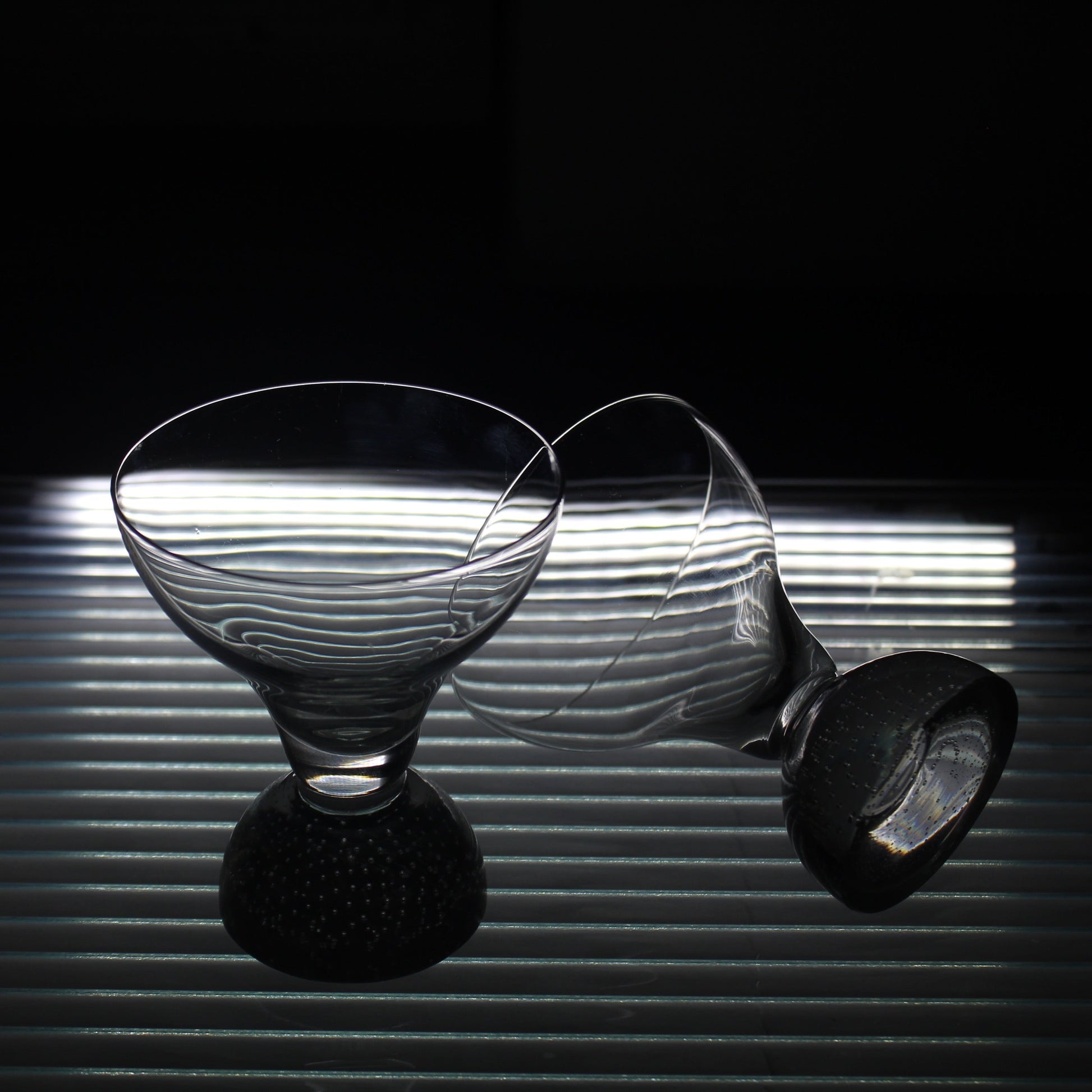 Two glass goblets on a reflective surface with a dark background