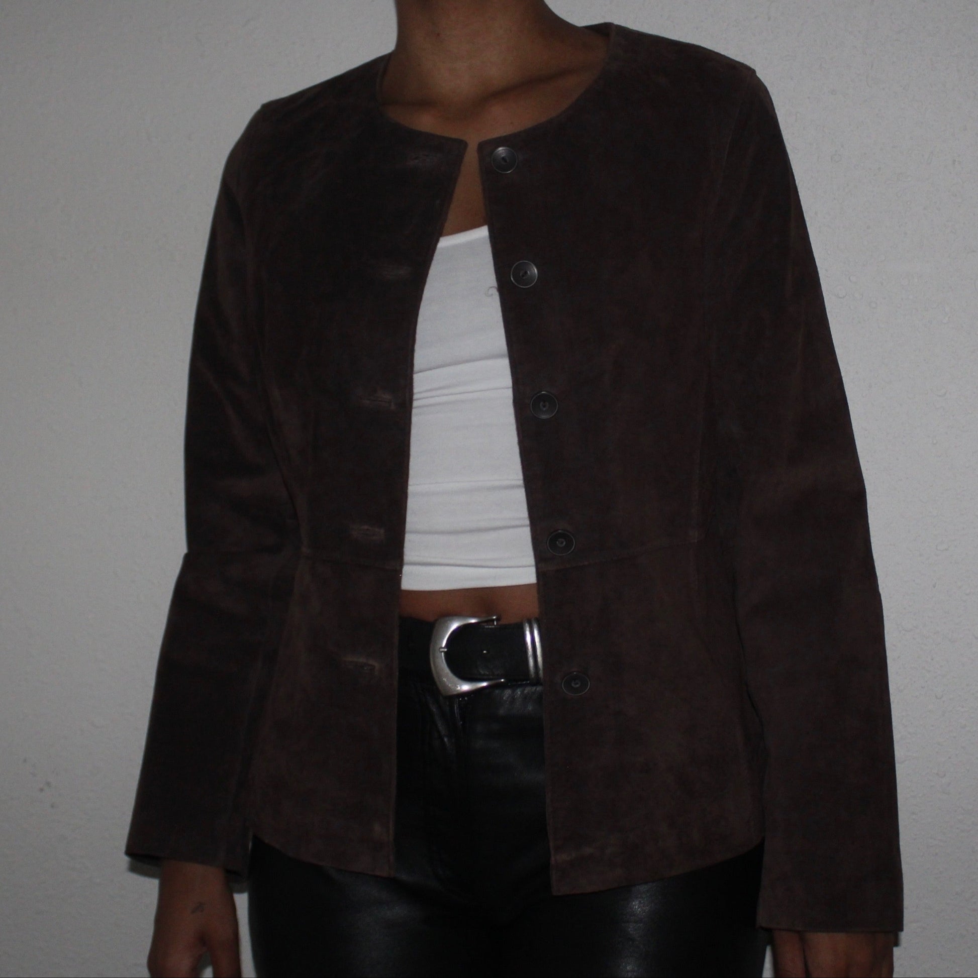 Brown suede jacket over a white top and black leather pants on a plain background