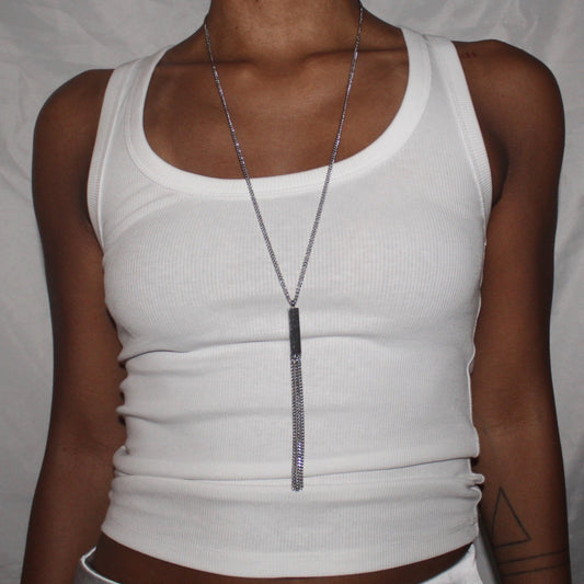 Person wearing a white tank top and a long necklace against a plain background