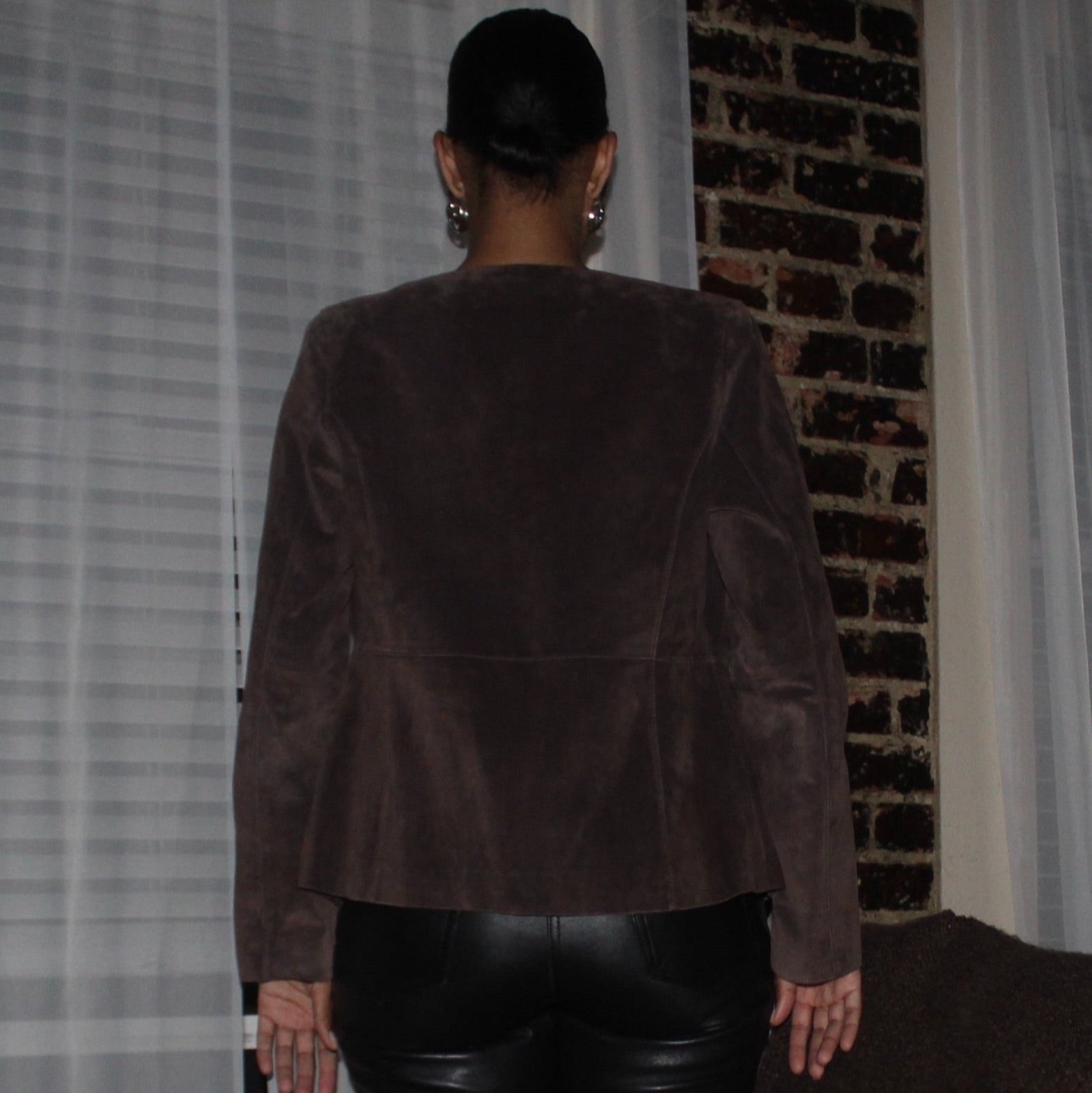 Person wearing a brown suede jacket in front of a brick wall.