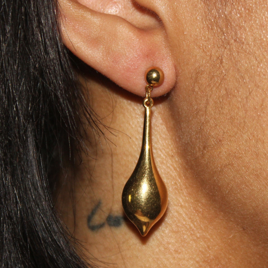 Gold earring worn by a person with dark hair and visible earlobe.