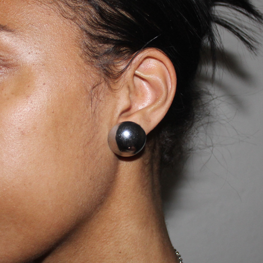 Close-up of an ear wearing a black spherical earring against a neutral background
