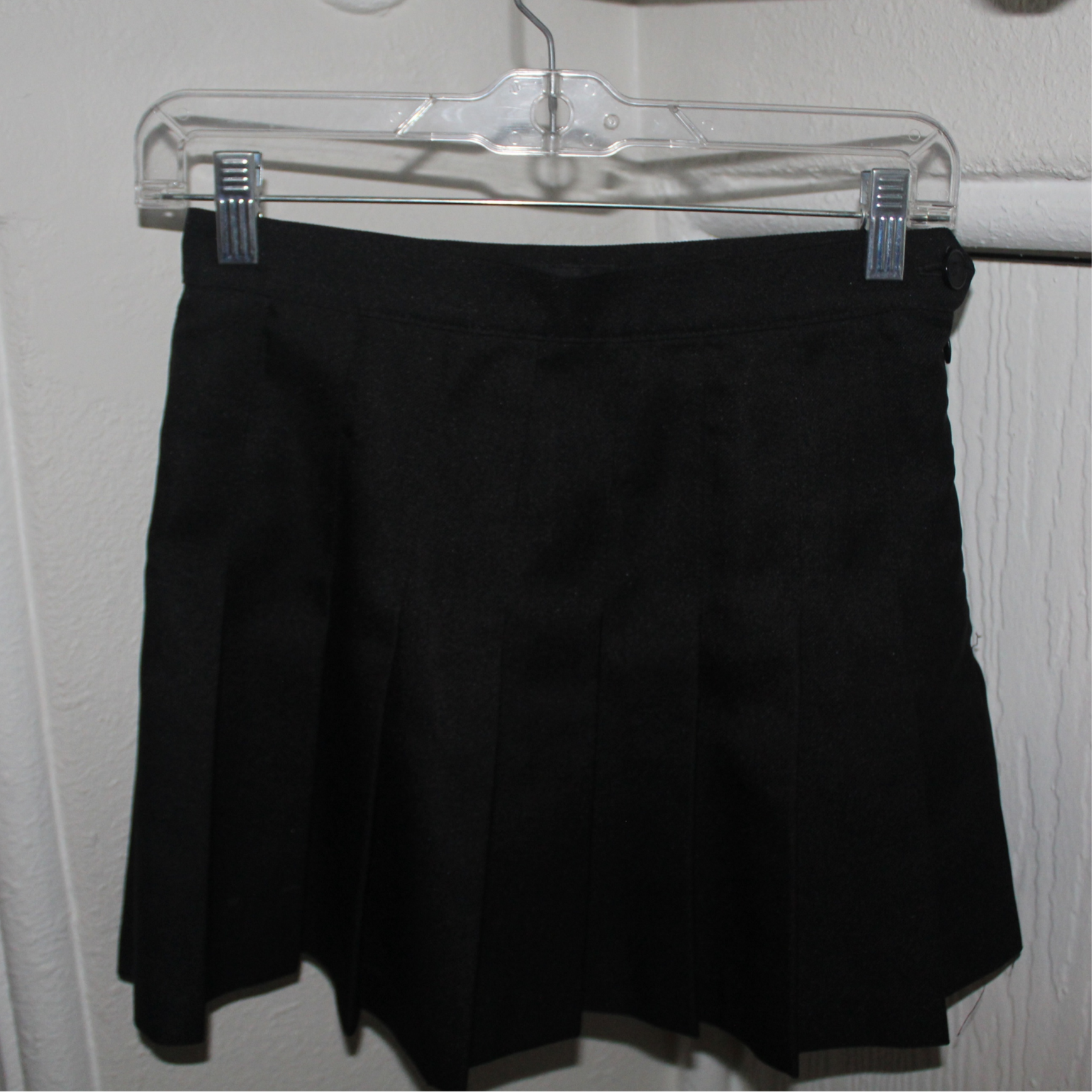 Black shorts on a clear hanger against a white wall